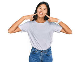 Beautiful young asian woman wearing casual white t shirt smiling cheerful showing and pointing with fingers teeth and mouth. dental health concept.