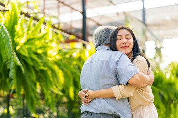 Happy Asian family hanging out together on summer vacation. Attractive adult woman hugging elderly father during shopping at plant shop street market. Father and daughter relationship concept.