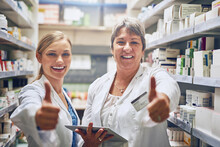 We Are The Medication Specialists. Shot Of Pharmacists Showing Thumbs Up In A Isle.