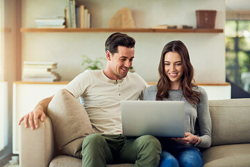 Wall Mural - The online experience is even better when its shared. Shot of a happy young couple using a laptop together on the sofa at home.