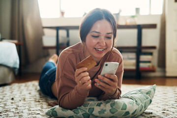 Poster - Same day shipping Sold. Shot of a young woman using a smartphone and credit card at home.