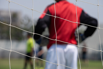 Boy elementary local soccer team practicing tactics and drilling on a green pitch with their coach after a school day in the evening. Selective focus on the field and net. A local sport youth centre.