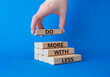 Do more with less symbol. Concept words Do more with less on wooden blocks. Businessman hand. Beautiful blue background. Businessman hand. Business and Do more with less concept. Copy space.