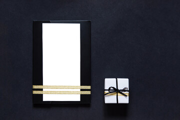 Sticker - black envelope mockup, shot from the top on a black background with copy space. Tied with a gold ribbon. Gift box with ribbon. white blank card for text. Business invitation, Father's Day.