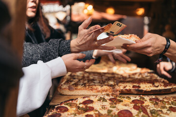 Unrecognizable woman's hands paying for a slice of freshly made artisan pizza at a Spanish medieval market street stall.