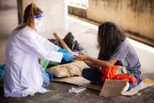 Health Workers In Uniforms, Gloves And Protective Masks While Helping The Homeless. Depressed Homeless Poor Help And Hope Concept