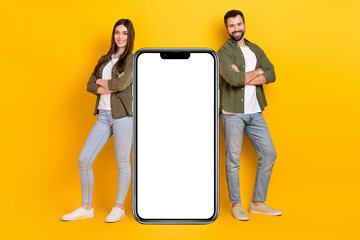 Poster - Full body image of two cool confident woman and man posing near big smartphone ad isolated on yellow color background