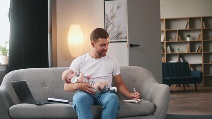 Sticker - Busy man using laptop and writing in document by pen. Father with his little baby is at home.