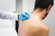 Espalda de paciente siendo examinada por dermatólogo con guantes para observación de lunares