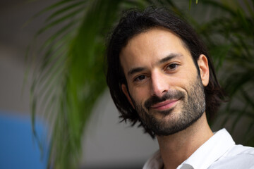 Wall Mural - portrait d'un jeune homme de 30 ans beau et souriant. En arrière plan, il y a des plantes vertes et un bureau confortable