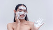A studio portrait with a white backdrop shows a Filipina transwoman enjoying applying the foamy soap as she gently exfoliates the dirt on her face. Isolated on a white background. Cosmetics endorser.