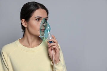 Poster - Sick young woman using nebulizer on grey background, space for text