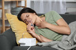 Sick young woman using nebulizer on couch at home