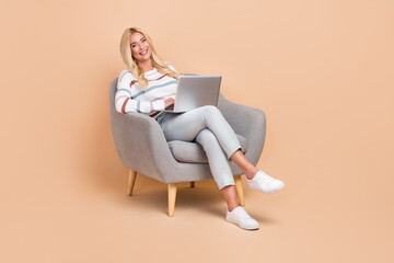 Sticker - Full length photo of cheerful blonde hair girl sitting chair use netbook for remote work freelance project manager isolated on beige color background