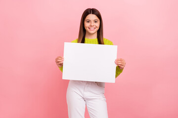 Wall Mural - Photo portrait of lovely teen lady showing white paper sheet empty space dressed stylish green clothes isolated on pink color background