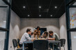 © Maskot - Multiracial male and female colleagues writing while discussing in meeting at illuminated board room