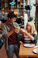 Wall Mural - Young cheerful couple toasting while eating cake in cafe.