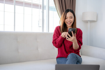 Wall Mural - Happy young Asian business woman successful excited raised hand rejoicing with smartphone at home.