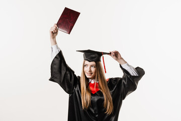 Wall Mural - Graduate girl is graduating college and celebrating academic achievement. Happy girl student in black graduation gown and cap raises masters degree diploma above head on white background.