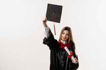 Wall Mural - Graduate girl is graduating high school and celebrating academic achievement. Masters degree diploma in hands. Happy student in black graduation gown and cap is smiling on white background.