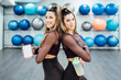 Sporty twin sisters posing with vitamin shake in gym