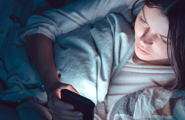 Young girl in a bed with a phone at night.