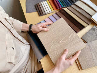 Top view: male interior designer chooses finishes for a house, examines samples of wood and fabrics. Concept: the architect selects the color of textiles and samples of materials for floor