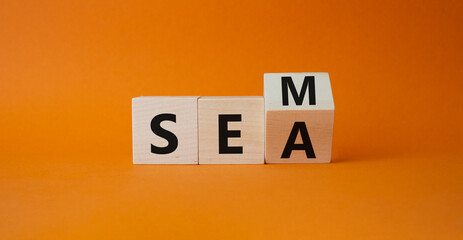 SEM vs SEA symbol. Turned wooden cubes with words SEA and SEM. Beautiful orange background. Business and SEM vs SEA concept. Copy space