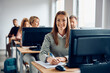 © Drazen - Happy mid adult student writes notes while learning on desktop PC in classroom.