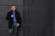 © Татьяна Волкова - Portrait of young attractive smiling employee of architectural bureau, standing against dark gray wall of city building