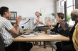 © sofiko14 - Multi ethnic male partners in formal clothes applauding together while sitting at office. Competent financiers businessmen with modern gadgets on table celebrating successful completion of project.