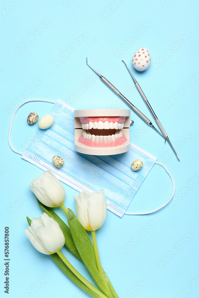 Jaw model with dental tools, medical mask. Easter eggs and tulips on blue background