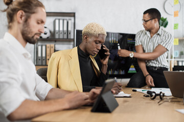 Wall Mural - Focused african man speaks on the phone while his male colleagues listening speech of african american businessman. Company managers working at office room. Deadlines concept.