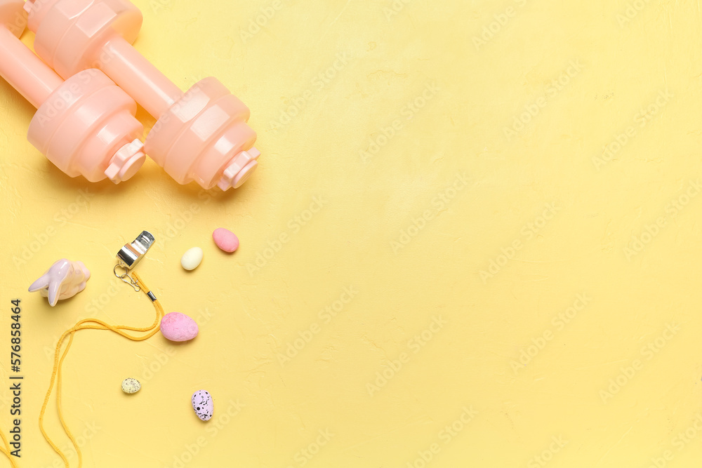 Dumbbells with whistle, Easter eggs and rabbit on yellow background