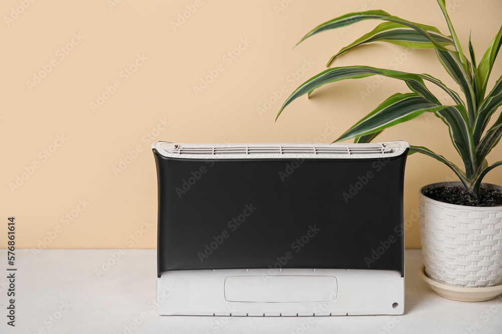 Air purifier and houseplant on table near beige wall