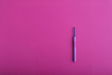 A Blue Shiny Crochet Hook With A Light Purple Plastic Handle Is Positioned As The Main Object Against A Large Bright Pink Textured Background. Copy Space View. Knitting, Needlework