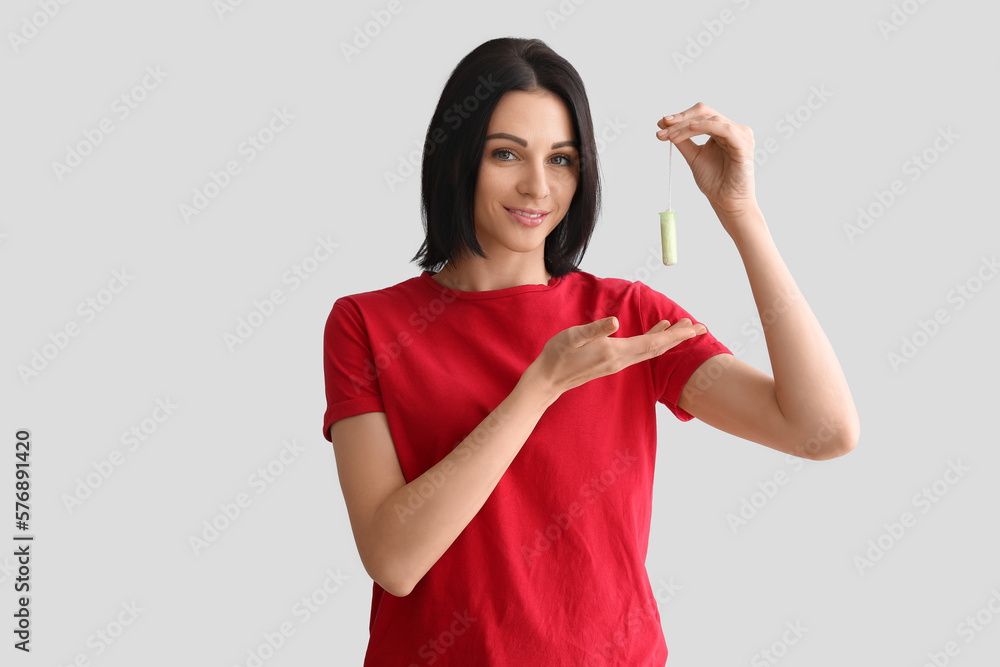 Young woman with tampon on grey background