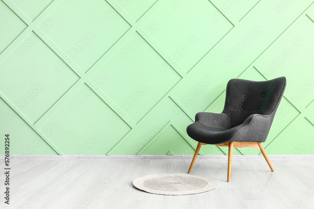Stylish grey armchair and wicker rug near green wall
