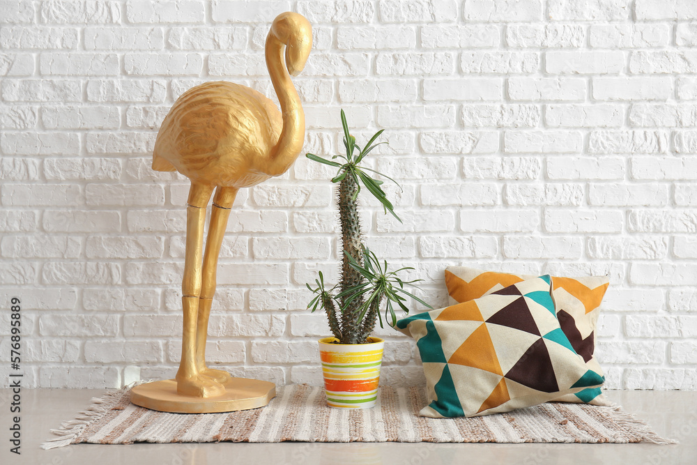 Green cactus, decorative flamingo and pillows near white brick wall