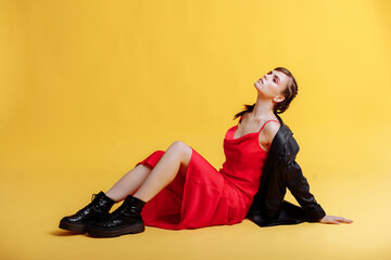 Portrait of a beautiful woman model in a red dress with braids and bright makeup. Model portrait of a young beautiful fashion model posing on a yellow background.