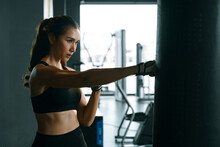 Young Woman Practicing Boxing At The Gym, She Wears Boxing Gloves And Hits A Punching Bag.