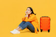 Young sad worried upset woman wear summer casual clothes sit near suitcase isolated on plain yellow background. Tourist travel abroad in free spare time rest getaway. Air flight trip journey concept.