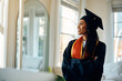 © Drazen - Confident African American female student in graduation gown at home.
