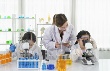 woman scientist as a mentor is teaching the students asian children in scientist uniform trying to u