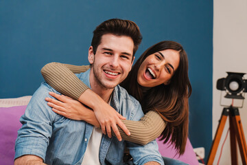 Close up portrait of happy caucasian young couple hugging and smiling together in a couch at home. Beautiful brunette wife embracing her husband resting in a sofa indoors. High quality photo