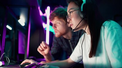 Wall Mural - Smiling Asian woman gamer playing RPG video game and talking with her ginger friend on a championship. Stylish Neon Cyber Games