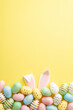 canvas print picture - Easter celebration concept. Top view vertical photo of colorful easter eggs and easter bunny ears on isolated yellow background with empty space