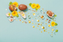 Easter Chocolate Egg With Golden Confetti And Spring Flowers On Blue Mint Paper Background