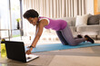 © Wavebreak Media - Smiling mid adult african american woman using laptop while practicing online yoga at home