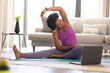 © Wavebreak Media - Mid adult african american woman practicing online yoga in living room at home